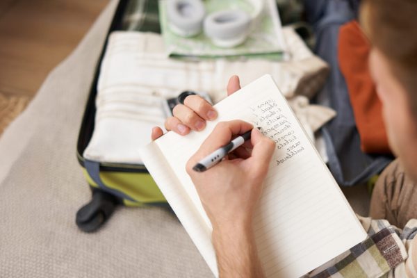 Close up portrait of man packing suitcase, making notes, check-list of items he wants to take on holiday, packing luggage.